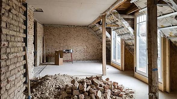 Dachgeschoss mit freigelegter Backsteinwand und Bauschutt nach Rückbauarbeiten